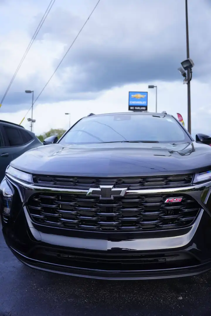 Direct front view of a black Chevrolet Trax RS crossover parked on the lot, showcasing its glossy black mesh grille, black bowtie emblem, RS badging, and the blue McFarland Chevrolet dealership sign in the background