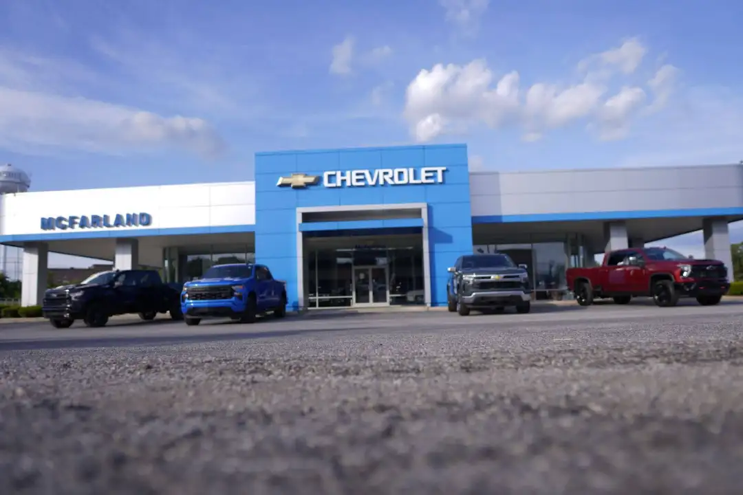 Wide low-angle view of the McFarland Chevrolet dealership building in Maysville, KY, featuring a lineup of new Chevrolet pickup trucks parked out front under a bright blue sky