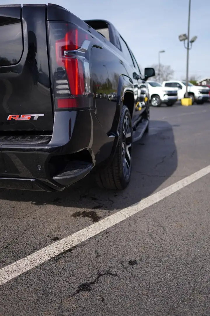Rear angle view of a black Chevrolet Silverado EV RST truck parked on a dealership lot, highlighting its modern taillight design and RST badging
