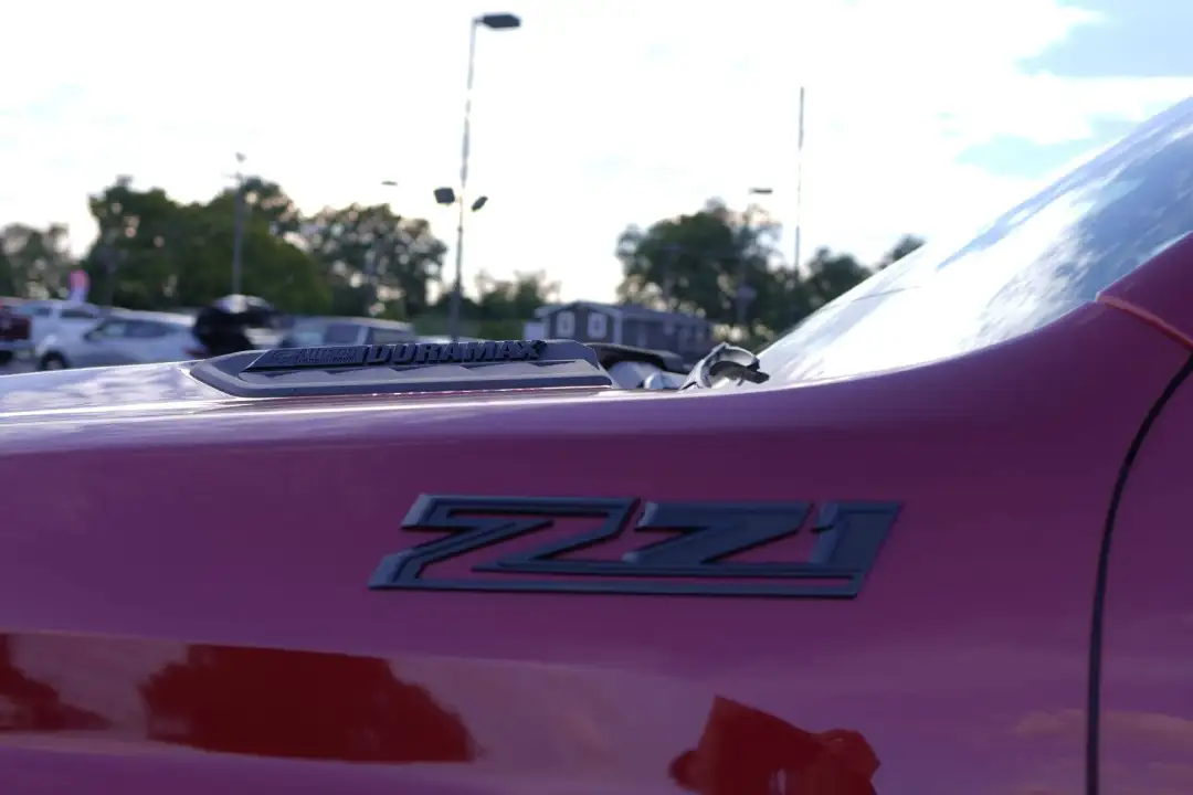 Close-up of a matte black Z71 off-road emblem on a red Chevrolet Silverado 2500HD truck fender, featuring the Duramax diesel hood badge at McFarland Chevrolet