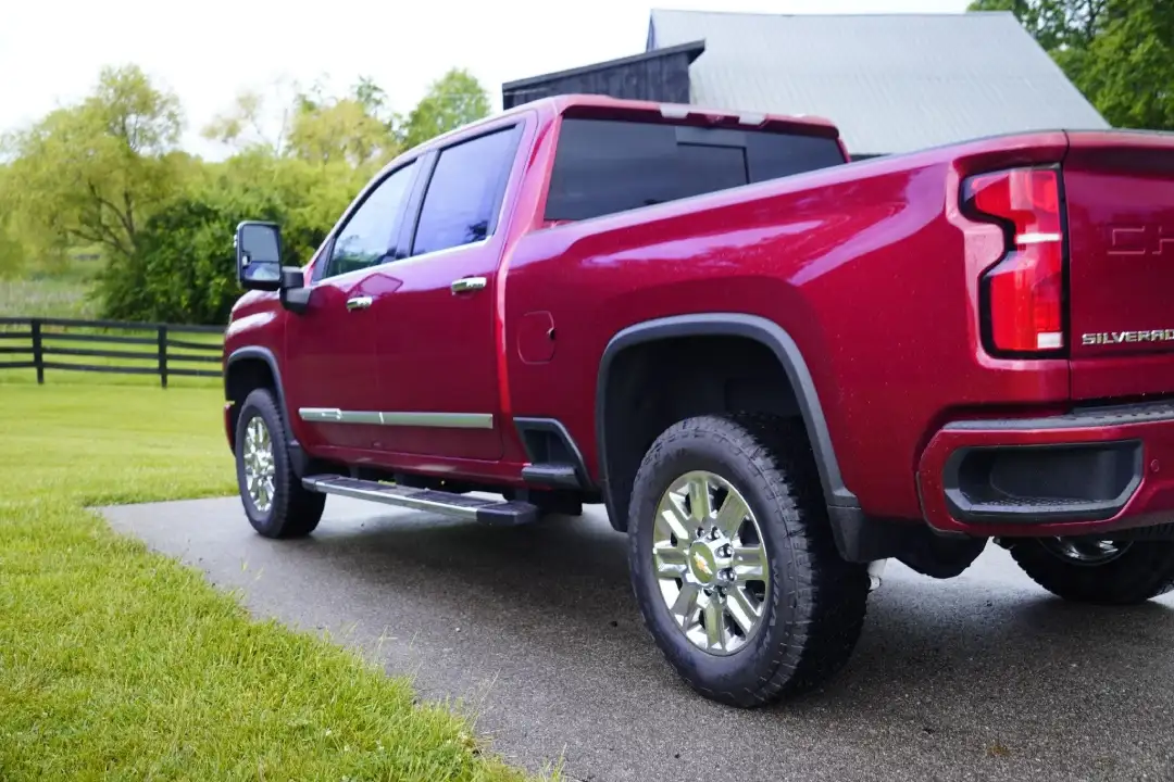 Rear three-quarter view of a cherry red Chevrolet Silverado 2500HD Duramax diesel truck parked on a farm driveway, illustrating real-world work capability at McFarland Chevrolet