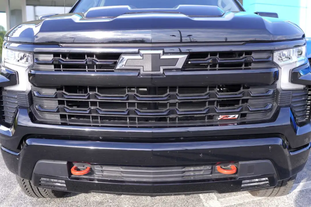 Front grille close-up of a black Chevy Silverado Trail Boss featuring the red Z71 badge and signature red recovery tow hooks