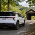 2027 Chevrolet Traverse on a winding Kentucky county road approaching a historic covered bridge in late summer