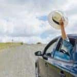 A person holding their hat out of a car window