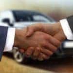 Two men shaking hands in front of a car