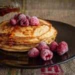 A plate of pancakes topped with syrup and raspberries