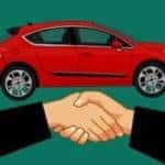 Two people shaking hands in front of a red car
