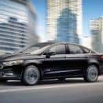 A black 2017 Ford Fusion is driving past city buildings.
