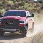 Red 2020 RAm 1500 kicking up dust as it drives in the desert
