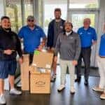 An image displaying six people standing around a pile of boxes of sports equipment smiling at the camera standing in the used car department at Preston Hood Chevrolet