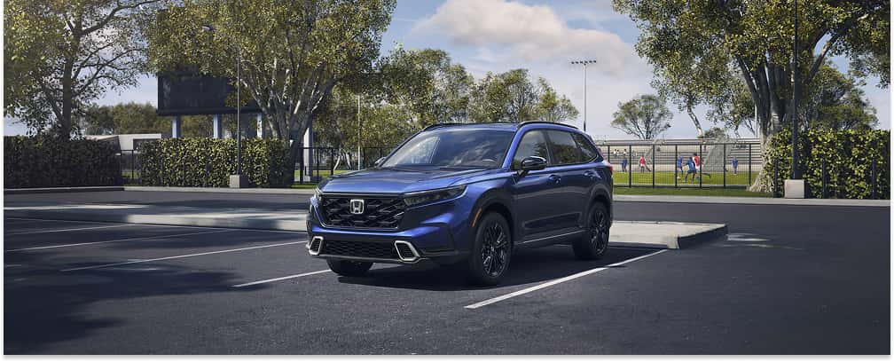 The 2026-honda-cr-v-overview-blog-post.jpg image showcases a front three-quarter view of a blue 2026 Honda CR-V parked in an outdoor parking lot with trees and a sports field in the background.