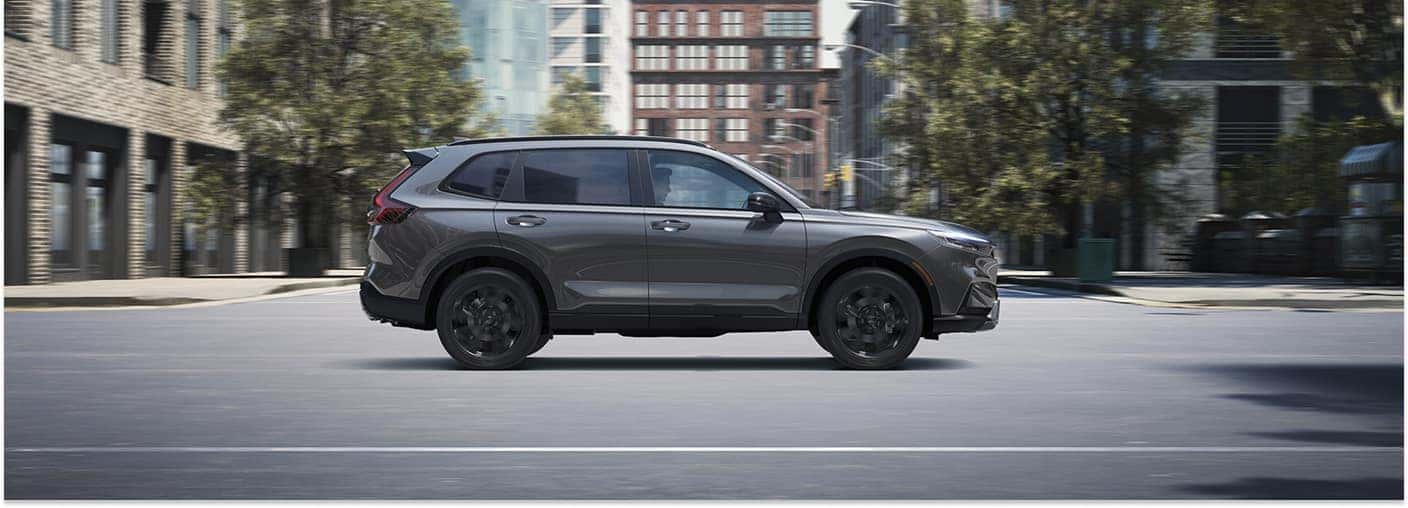 Gray 2026 Honda CR-V driving on a city street, side profile view.